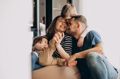 Foreldre omfavner sine to glade barn hjemme, symboliserer barnerådgivning og familie- og foreldreveiledning for et støttende og nærende miljø.