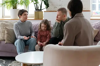 Bildet viser et par i intens diskusjon med terapeuten, mens en jente sitter stille mellom dem