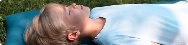Bildet viser en gutt som ligger på gresset med en pute og soler seg