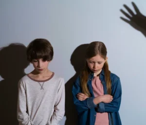 To triste barn står mot en vegg med en truende skygge bak seg, som symboliserer barnemishandling og omsorgssvikt som truer barns helse og trygghet.