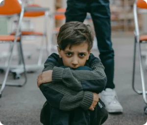 Et barn som sitter på bakken med armene rundt knærne, ser alvorlig og tankefull ut, et visuelt uttrykk for psykiske utfordringer hos barn
