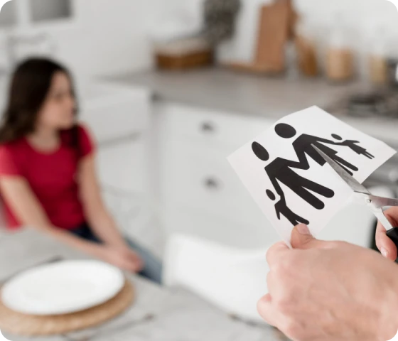 En person som klipper en familieillustrasjon med saks, mens et barn sitter i bakgrunnen, som symboliserer skilsmisse og de emosjonelle utfordringene for barn.