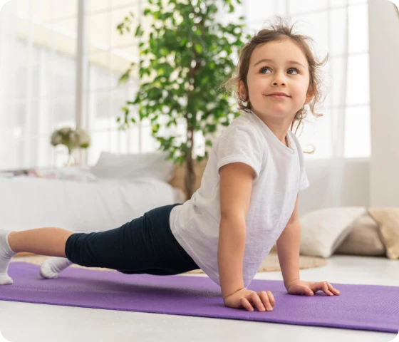 Et lite barn gjør en strekkøvelse på en yogamatte hjemme, som illustrerer temaet Barn og fysisk aktivitet: En viktig gave for livet.